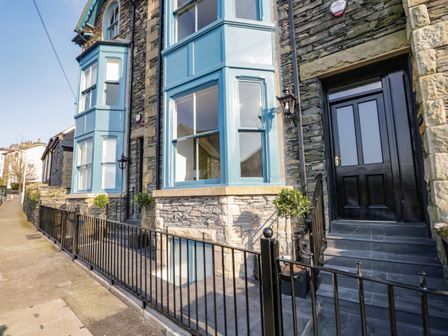 Exterior view of a stone house with blue bay windows black door and metal railing at The Willows in Windermere