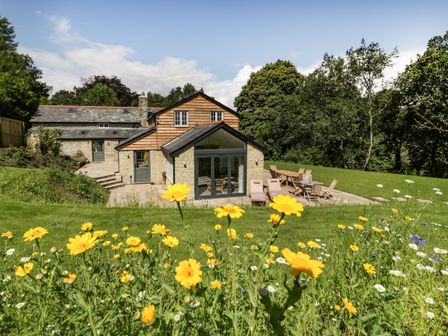 A garden with yellow and white flowers in front of a stone and wood house with patio furniture at Hillside Cottage in Shaftesbury