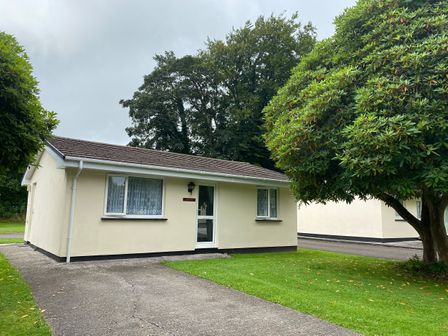 A single-story house with two windows and a glass door near a large tree and a driveway at Lands End in Liskeard near St Cleer