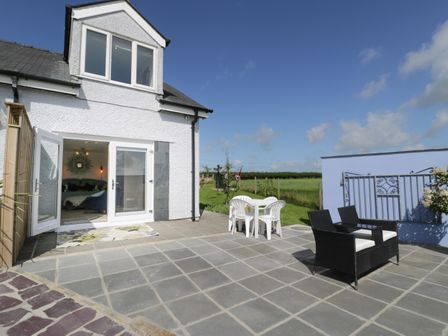 An outdoor patio with two chairs and a table near a white house with glass doors at Drws y Gorlan in Llanerch-y-medd