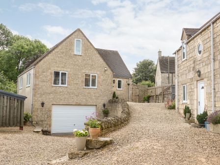 A stone house with a garage and gravel driveway with flower pots at Farm View Lodge in Painswick