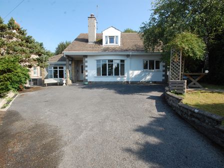 A house with a paved driveway and surrounding trees at Westwinds in Tenby