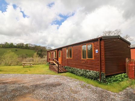A wooden mobile home with windows and a small ramp outside surrounded by grass and hills at Exe Valley Lodge in Bampton Devon