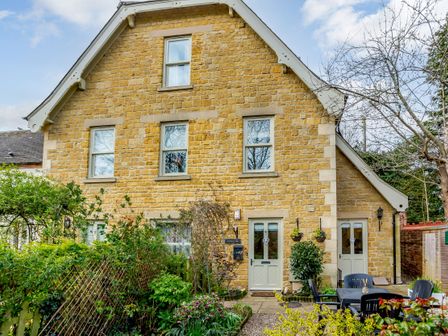 The front view of a two story stone house with multiple windows and doors and a garden with outdoor chairs and table at Jasmine Cottage Mickleton Gloucestershire