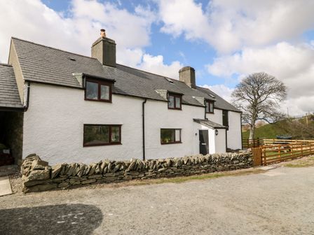A white farmhouse with a stone fence and wooden gate under a partly cloudy sky at Orsedd Wen Farmhouse in Betws-Y-Coed