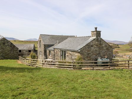 A stone cottage with slate roof and wooden fence surrounded by grassy fields at Orsedd Wen Cottage in Betws-Y-Coed