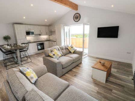 An open plan living room and kitchen with sofas a dining table and a wall mounted TV at Caban Y Mor in Amroth near Saundersfoot