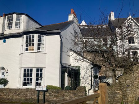 A white cottage with bay windows and a sign reading ford nos 1-16 in Dartmouth
