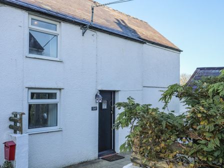Exterior view of a white house with two windows a black front door plants and a red mailbox at Oscars Pad in Brynsiencyn
