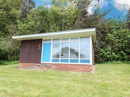 A small building with a blue door and large windows surrounded by grass and trees at Chalet 126a in Cromer