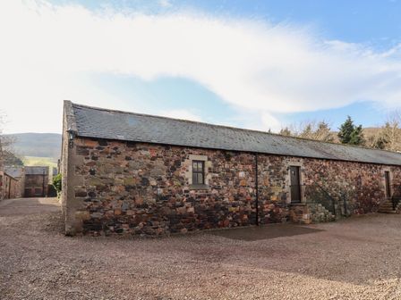An exterior view of a long stone building with a slate roof and staircases at Honeysuckle in Wooler
