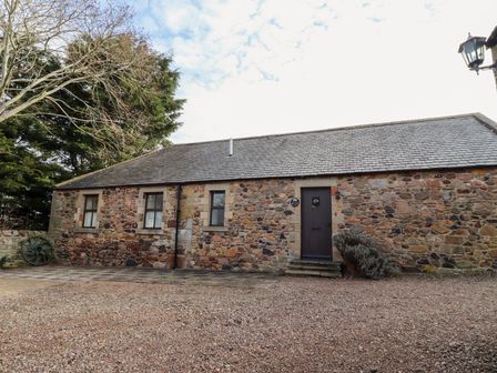 A stone cottage with three windows and a door with steps outside surrounded by trees at Cherryburn Cottage Akeld near Wooler