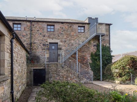 A stone house with metal stairs to an upper door and windows surrounded by bushes at Hollyhock in Akeld near Wooler