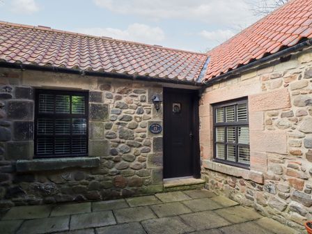 An exterior view of a stone building with two windows and a black door at The Smithy in Akeld near Wooler