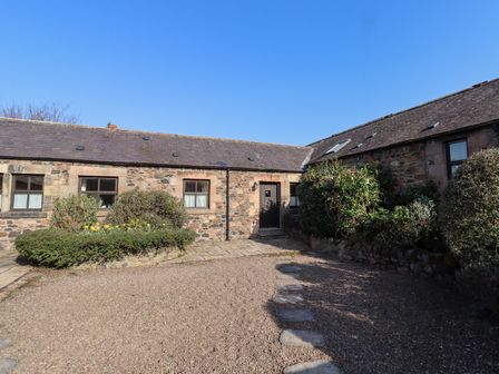 A gravel courtyard with stone cottages and bushes at Catkin Cottage in Akeld near Wooler