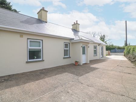An exterior view of a single-story house with a paved driveway and two chimneys at Lane Cottage in Ballycullane County Wexford