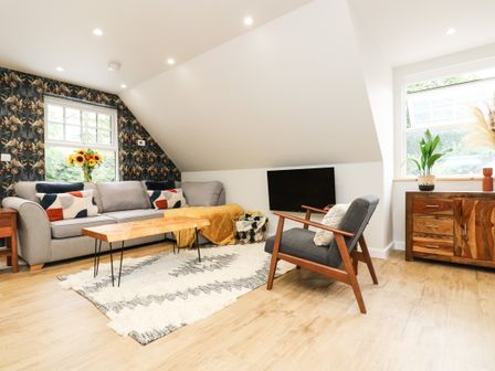 A living room with a gray sofa wooden coffee table patterned rug armchair and wooden cabinet at Robins Nest at The Shire Inn in Killivose near Camborne