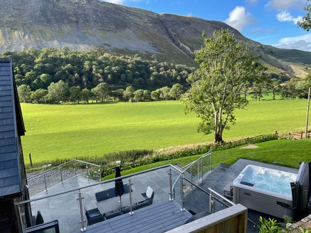 An outdoor patio with a dining table and chairs a hot tub a tree and green fields with hills in the background at Pennant Uchaf Pennant near Llanbrynmair