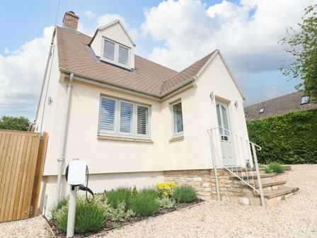 A cream house with a sloped roof gravel driveway and garden at Tawny Cottage in Fulbrook near Burford