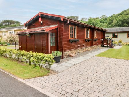A wooden house with a stone foundation and a paved driveway with a small hedge in front at Heritage Park in Stepaside near Kilgetty