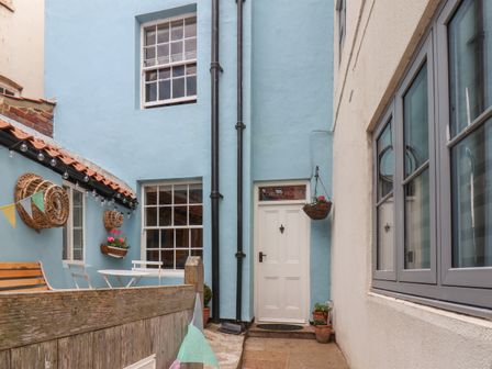 A narrow outdoor patio area with a white door and blue and white walls at Corner House Staithes