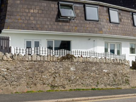 A house with a stone wall and white picket fence along a street at Fistral Drift in Newquay