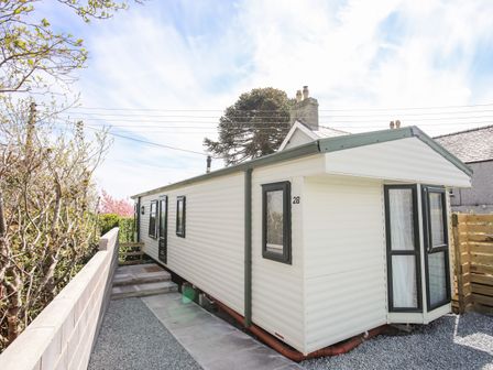A white caravan with black window frames and door next to a concrete wall and gravel pathway at Bryn Hyfryd Caravan in Dulas near Moelfre