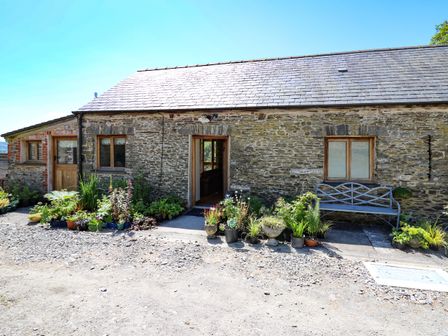 Stone cottage with wooden doors windows potted plants and a metal bench outside at Golwg Las in Pumsaint near Lampeter