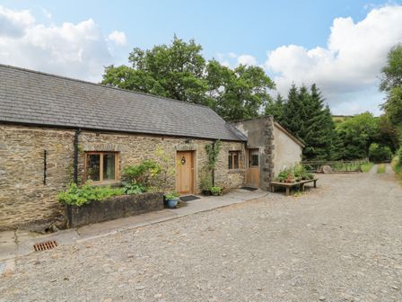 A stone building with wooden doors windows and plants outside beside a gravel road at Nant Glas in Pumpsaint near Lampeter