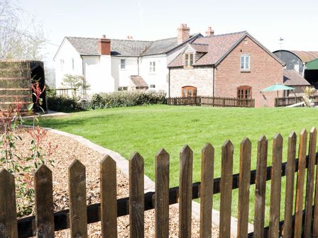 A fenced garden with green grass next to a brick and a white house at The Cider House in Leominster