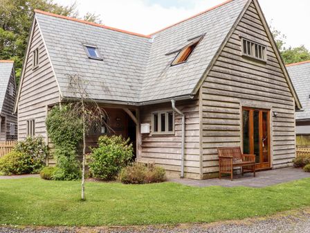 An exterior view of a wooden-clad house with a slate roof a bench on the patio and greenery at Bybrook Lodge in Davidstow near Camelford