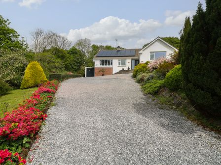 A house with solar panels on the roof surrounded by trees and a gravel driveway with flower beds at The Dingle in Wisemans Bridge near Stepaside