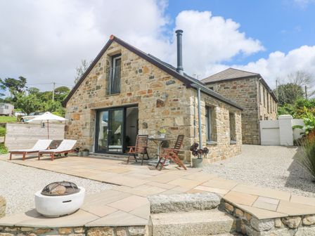 An outdoor patio with loungers chairs and a fire pit next to a stone house at Apple Blossom Barn in Gulval near Penzance