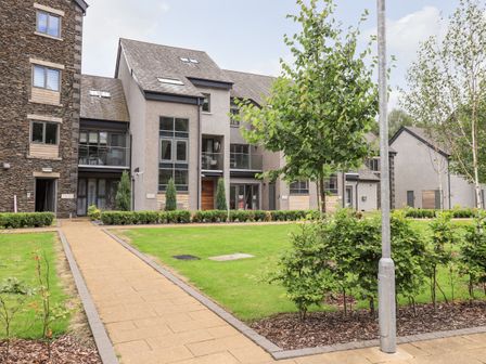 A pathway leading to modern apartment buildings with lawns and small trees at Rivers Edge in Newby Bridge