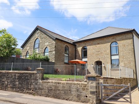 A stone building with arched windows and a fenced front yard with an orange umbrella at The Old Sunday School in Bream