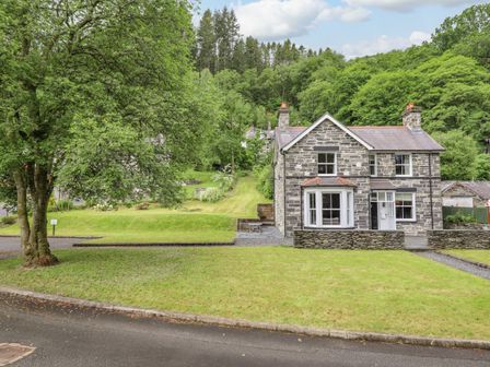A stone house with a front lawn and large tree beside a paved road at Craigside in Betws-Y-Coed