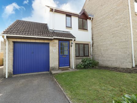 A house with a blue garage door and front door with a small lawn at 16 Mythern Meadow in Bradford-On-Avon