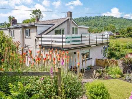A house with a garden and flowers in the foreground and hills in the background at Kavieng in Glangrwyney near Gilwern