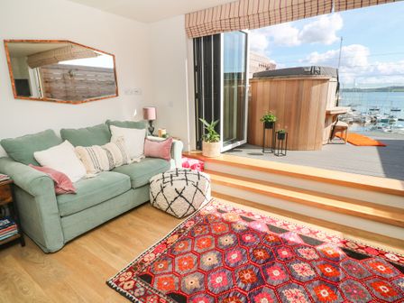 A living room with a green sofa white and pink cushions a patterned rug and an open door leading to a deck with plants and a hot tub overlooking boats at 16 Arwenack Street in Falmouth