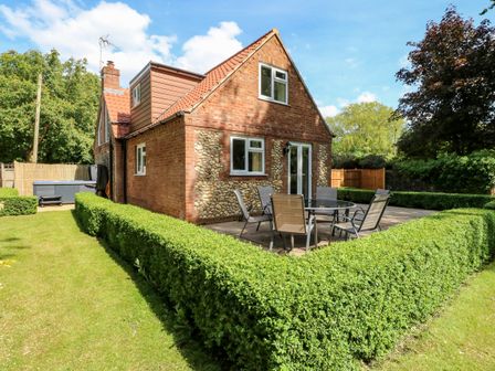 A brick and flint house with a tiled roof and patio furniture surrounded by trimmed hedges at Keepers Cottage in Beeston near Dereham