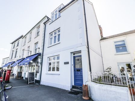 A street view of white buildings with blue doors and awnings and a sidewalk with a red post box at Ferriwais in Appledore
