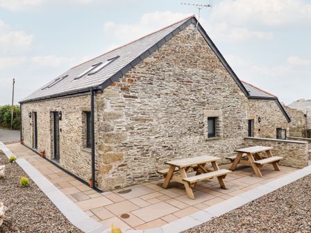 Exterior of a stone building with a slate roof and two wooden picnic tables on a paved patio at The Granary in Helland near Bodmin