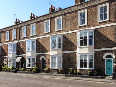 A row of brick terraced houses with bay windows and plants in front on a street at Seaside House in Weymouth