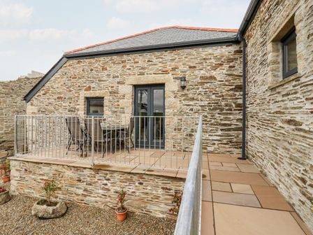 A stone building with a slate roof and a balcony with metal railing and outdoor chairs at The Hayloft in Helland near Bodmin