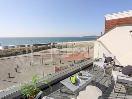 A balcony with two chairs a table with green apples and wine overlooking the sea at 26 Awel Y Mor in Pwllheli