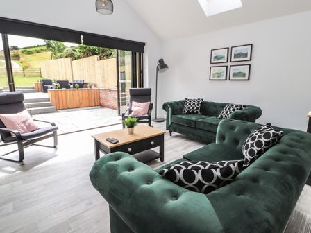 A living room with green sofas black and wooden chairs a coffee table and large glass doors opening to a patio at Ty Coch in Ruthin