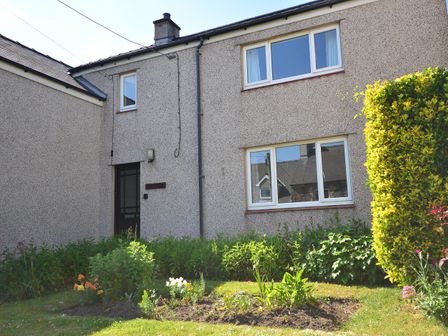 Exterior view of a two-story house with pebble-dash walls a garden with flowers and bushes at Idan House in Newborough
