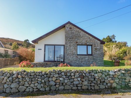 A single-story house with stone and white exterior walls a sliding glass door and a window with a stone wall in front at Hefo'r Grug in Mynytho near Abersoch