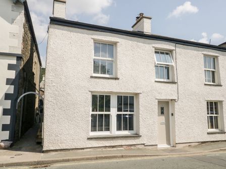 The exterior of a white painted terraced house with four windows and one door on a street at Hugill Cottage in Staveley near Windermere