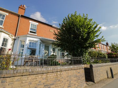 A row of brick houses with front gardens and a tree behind a low brick wall at Florence Villas in Worcester